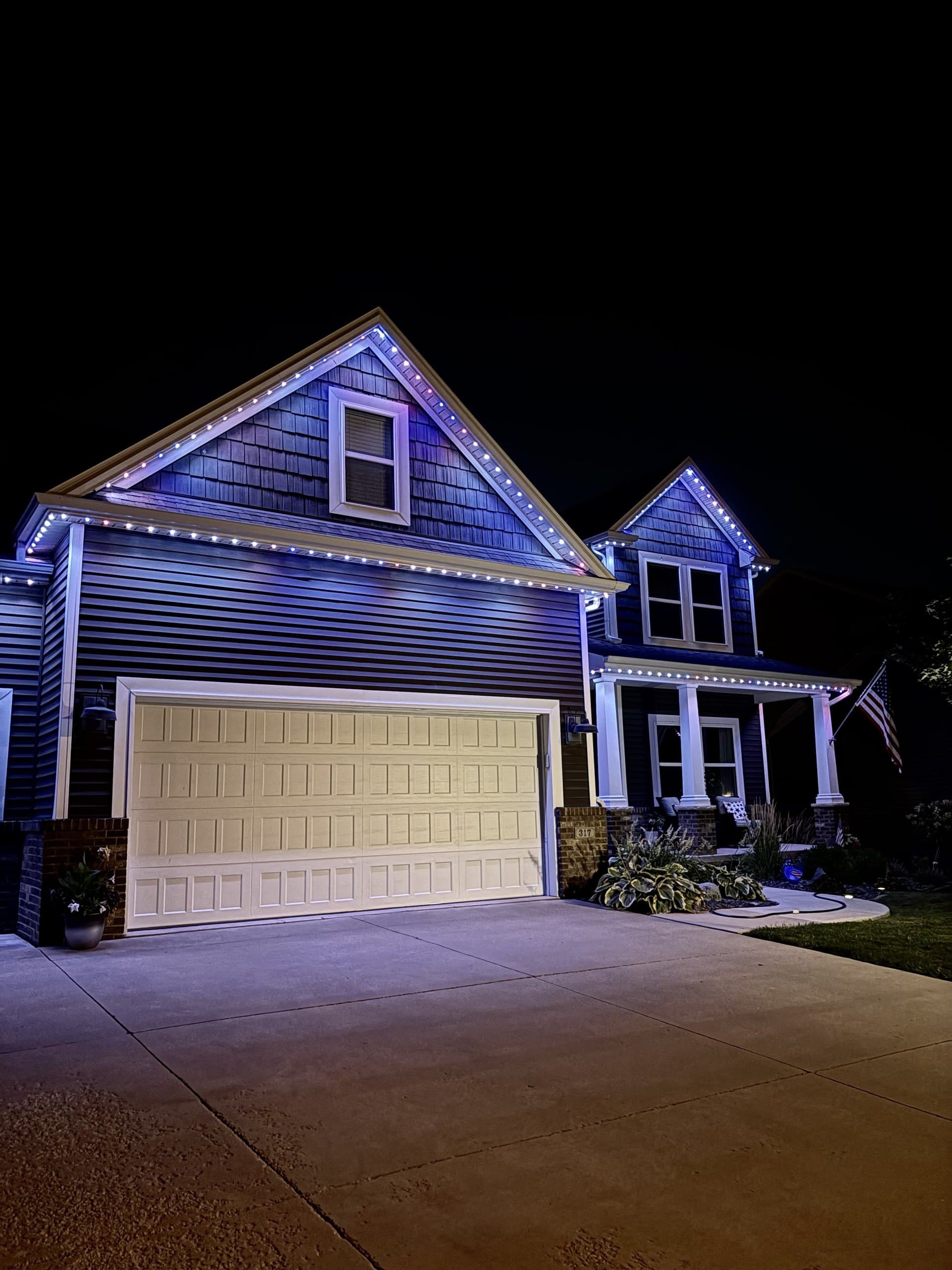 Craftsman home with blue and purple roofline lighting and a flag