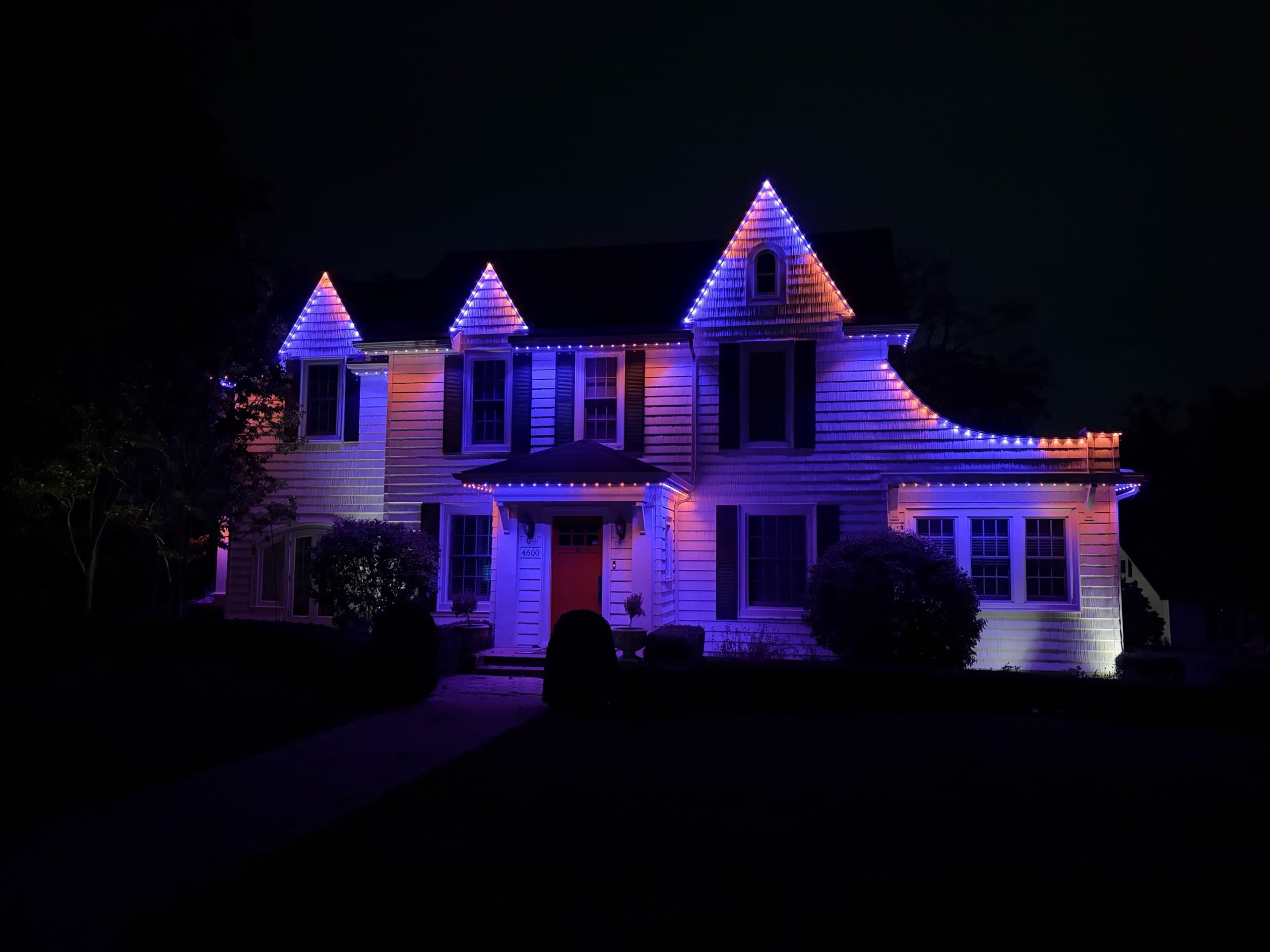 Colonial home at night lit with blue and purple permanent lighting