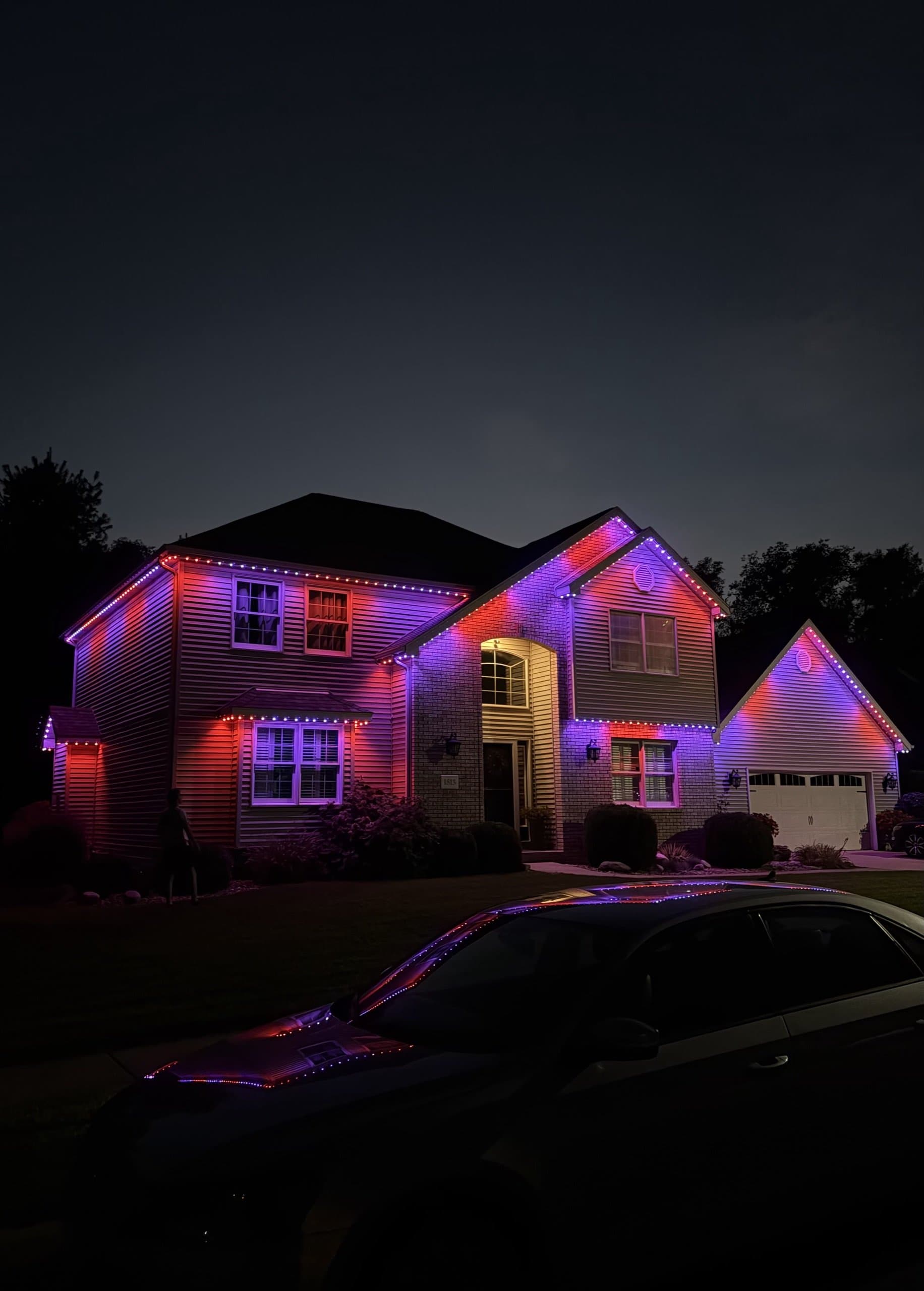 Two-story home at dusk lit in red and blue permanent lighting