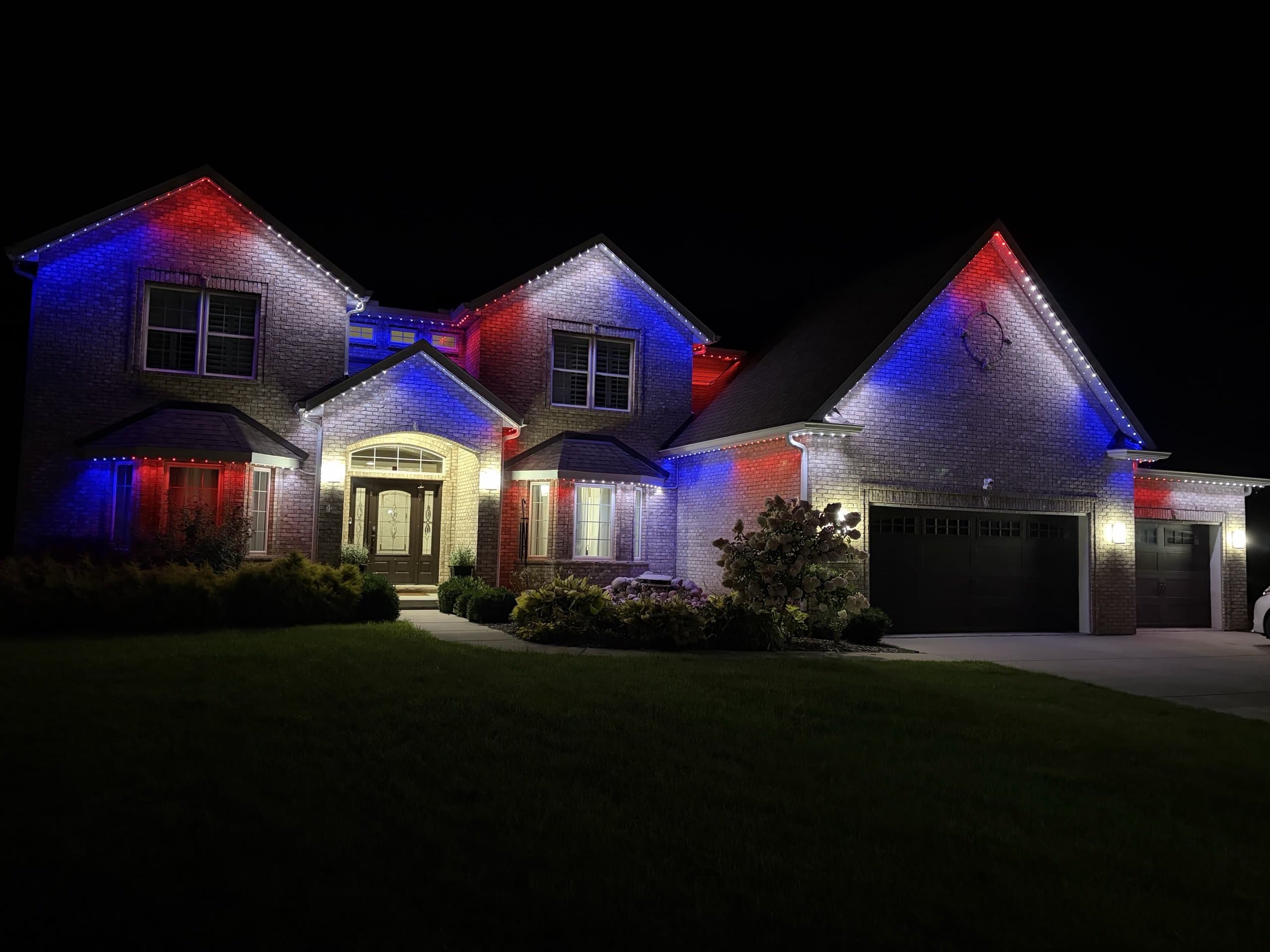 Large brick home at night lit edge-to-edge with red, white, and blue permanent LED lighting